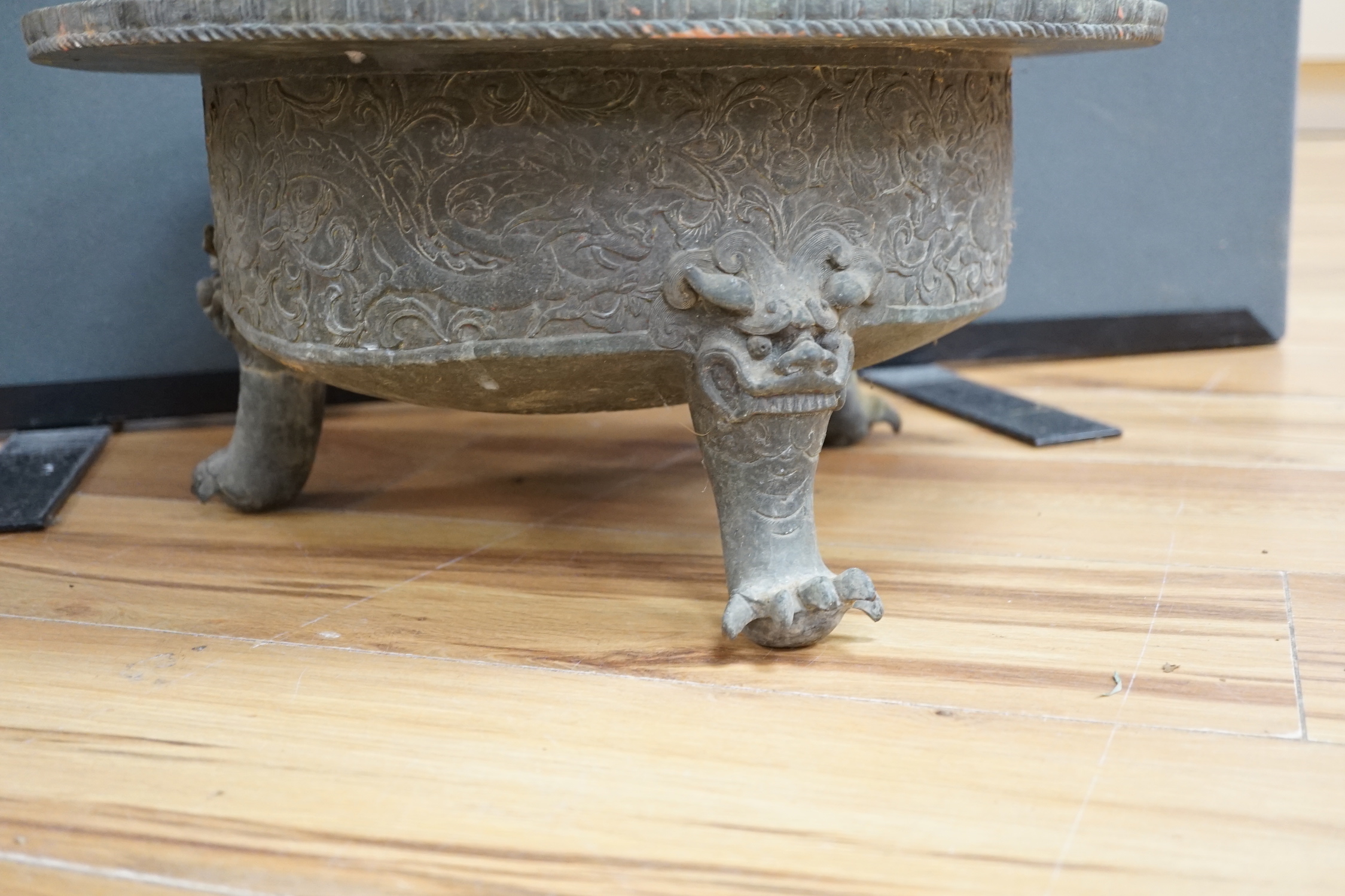 A large and heavy Chinese bronze tripod basin, Xuande mark but 19th century, the broad rim cast in relief with lions, brocaded balls and ribbons, the sides with dragons chasing flaming pearls, on three mythical beast hea